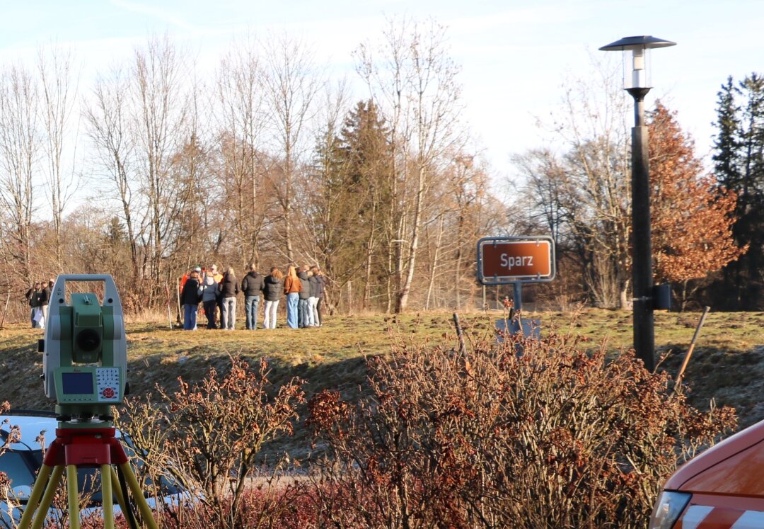 Eine Mädchengruppe steht auf einer Wiese und führt eine Grundstücksvermessung durch. Im Vordergrund steht ein Tachymeter.
